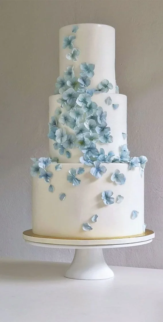 Elegant three-tier white fondant wedding cake decorated with a cascading trail of light blue hydrangea sugar flowers. Elegant three-tier white fondant wedding cake decorated with a cascading trail of light blue hydrangea sugar flowers.