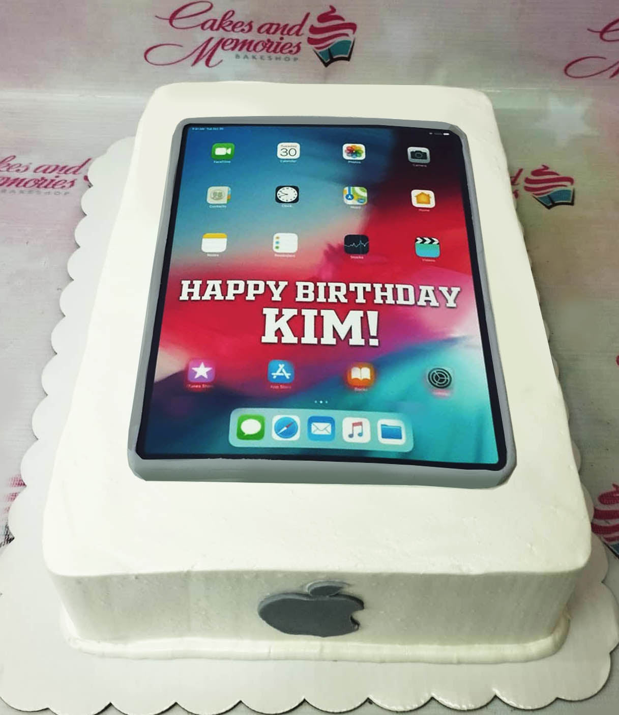 White rectangular iPad themed cake with a large edible printout screen displaying a colorful home screen and a Happy Birthday Kim message. White rectangular iPad themed cake with a large edible printout screen displaying a colorful home screen and a Happy Birthday Kim message.