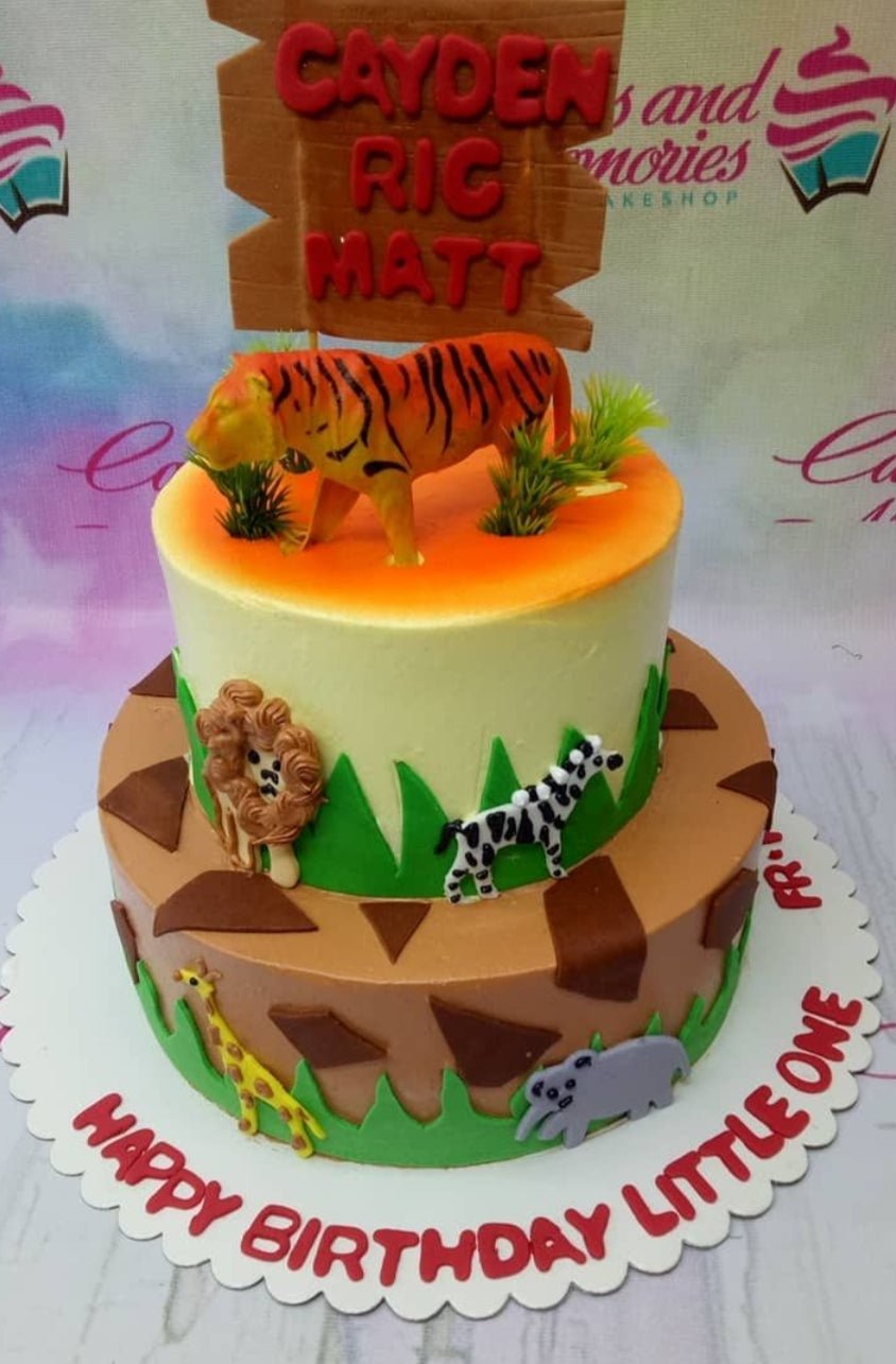 Two-tier jungle safari cake with a tiger topper, fondant animals like a lion, zebra, giraffe, and hippo, and a wooden-style name sign. Two-tier jungle safari cake with a tiger topper, fondant animals like a lion, zebra, giraffe, and hippo, and a wooden-style name sign.