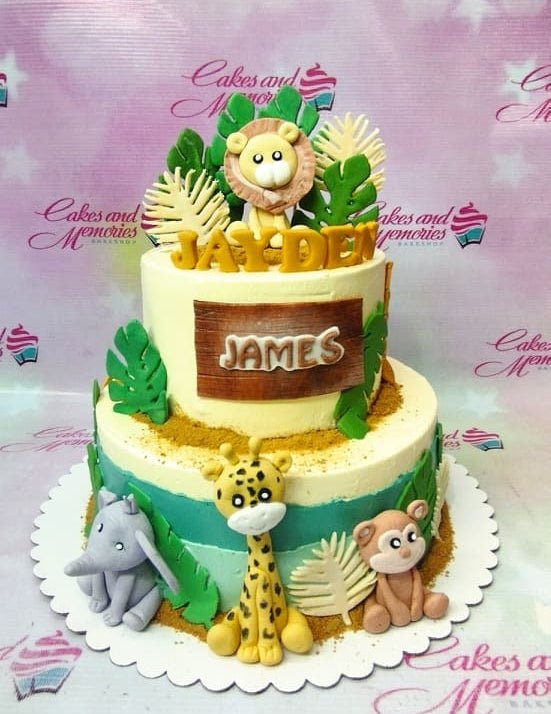 Two-tier jungle safari themed cake with fondant lion, giraffe, elephant, and monkey figures on a cream and teal base. Two-tier jungle safari themed cake with fondant lion, giraffe, elephant, and monkey figures on a cream and teal base.