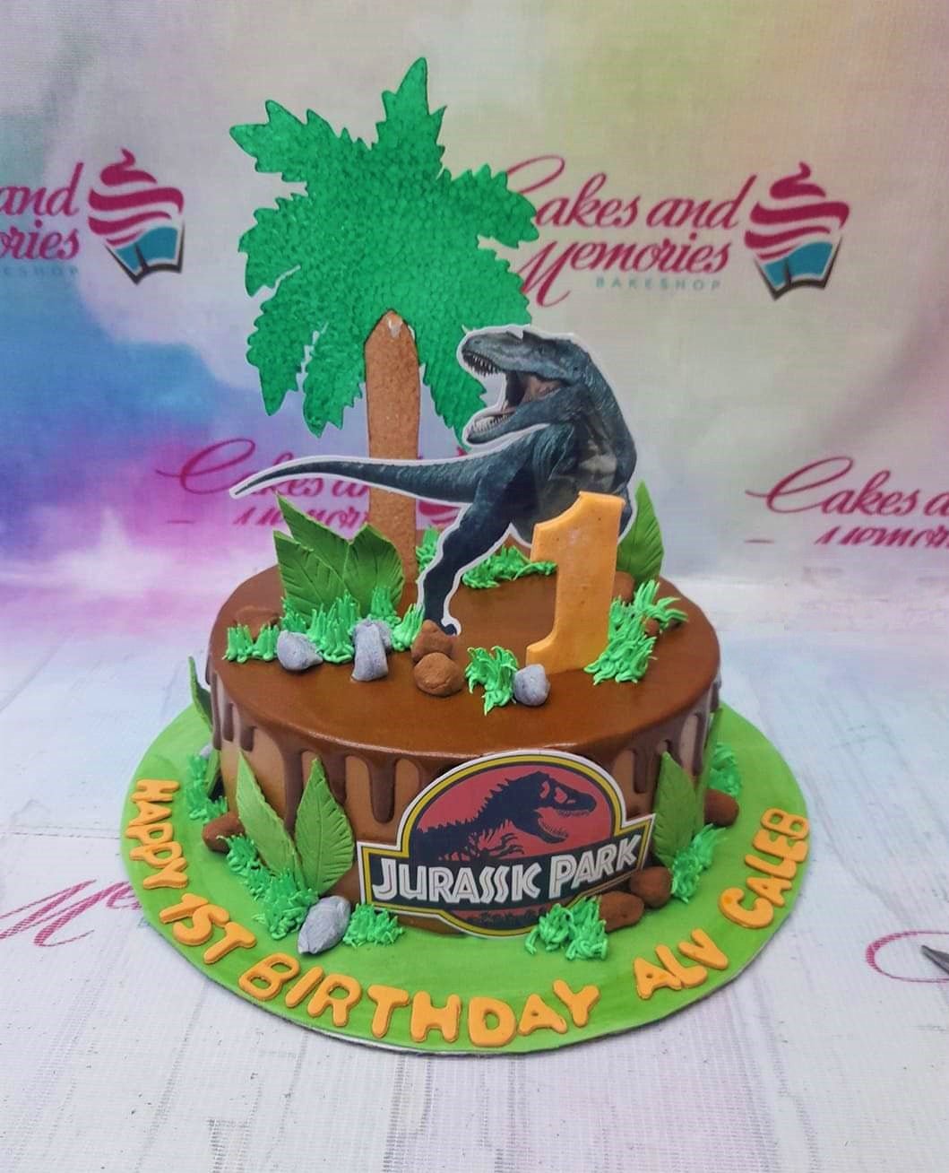 Jurassic Park themed chocolate drip cake with dinosaur printout, palm tree, and rocks on a green base board. Jurassic Park themed chocolate drip cake with dinosaur printout, palm tree, and rocks on a green base board.