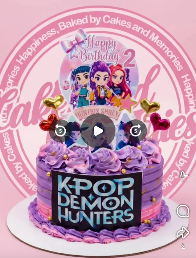 K-Pop Demon Hunters-Inspired Purple Birthday Cake Purple and pink K-Pop Demon Hunters themed cake with character printouts, gold hearts, and piped icing rosettes.