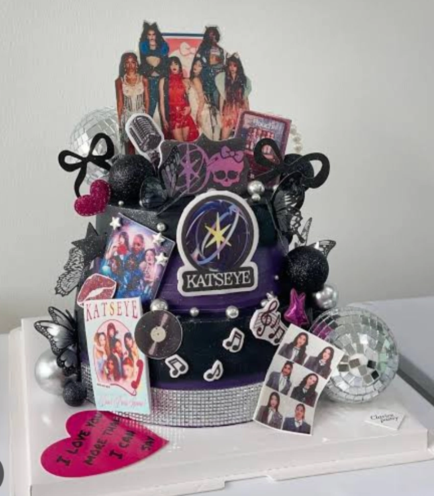 Black and purple Katseye K-pop themed cake with photo printouts, disco balls, and musical note decorations. Black and purple Katseye K-pop themed cake with photo printouts, disco balls, and musical note decorations.
