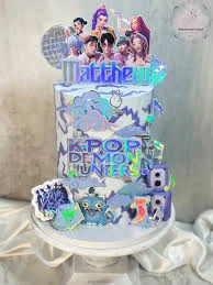 Tall white K-pop themed cake with holographic printouts of K-pop idols, speakers, and musical notes. Tall white K-pop themed cake with holographic printouts of K-pop idols, speakers, and musical notes.