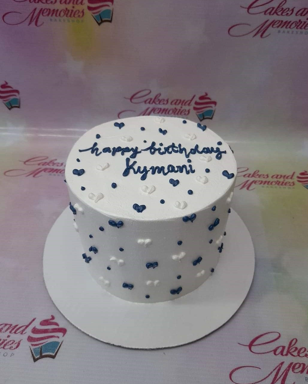 White minimalist birthday cake with navy blue and white heart-shaped icing dollops and navy blue piped message. White minimalist birthday cake with navy blue and white heart-shaped icing dollops and navy blue piped message.