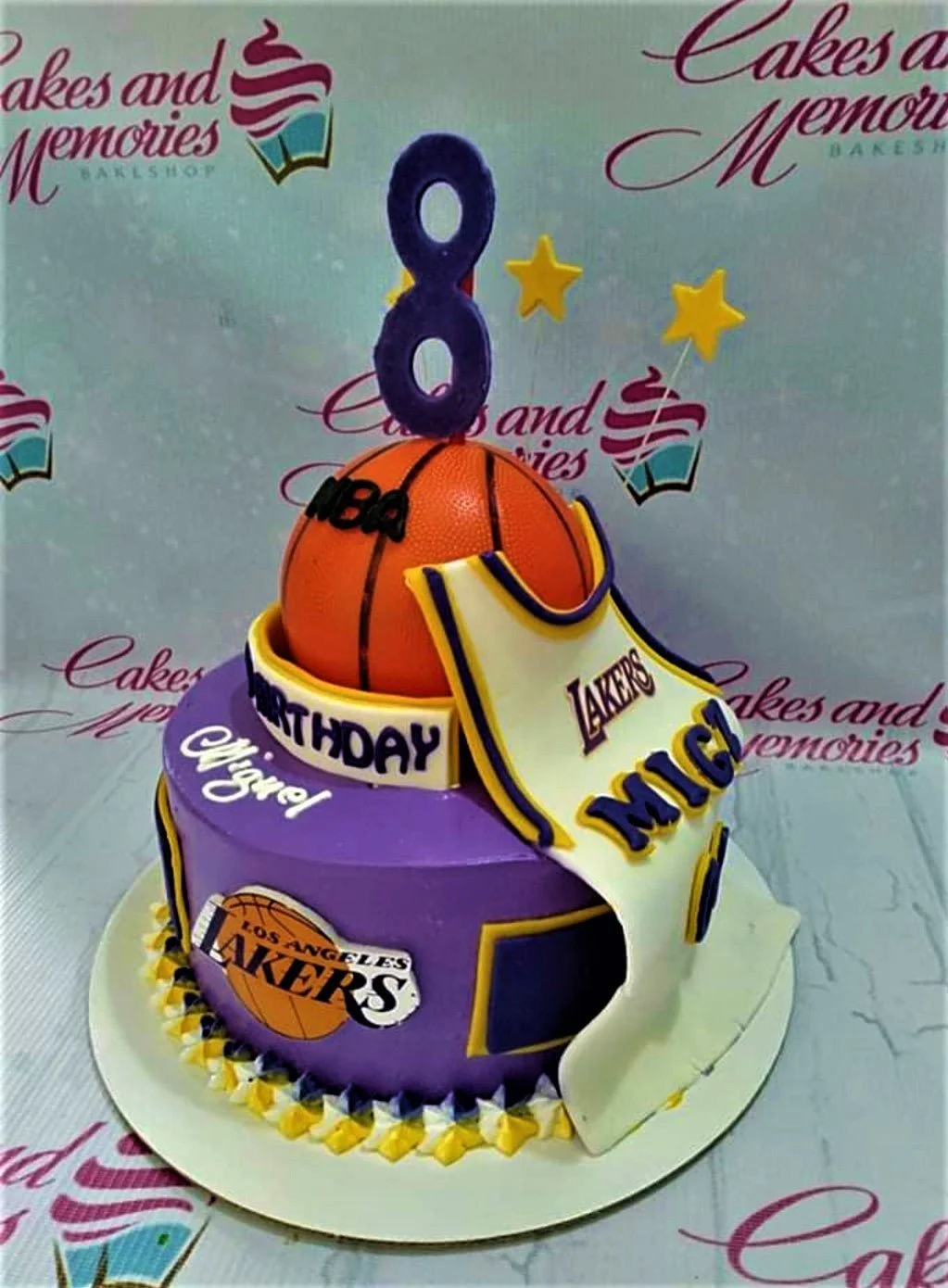 Lakers Basketball 2-Tier Cake Two-tier purple and white Los Angeles Lakers basketball themed cake with a large 3D basketball and jersey topper.