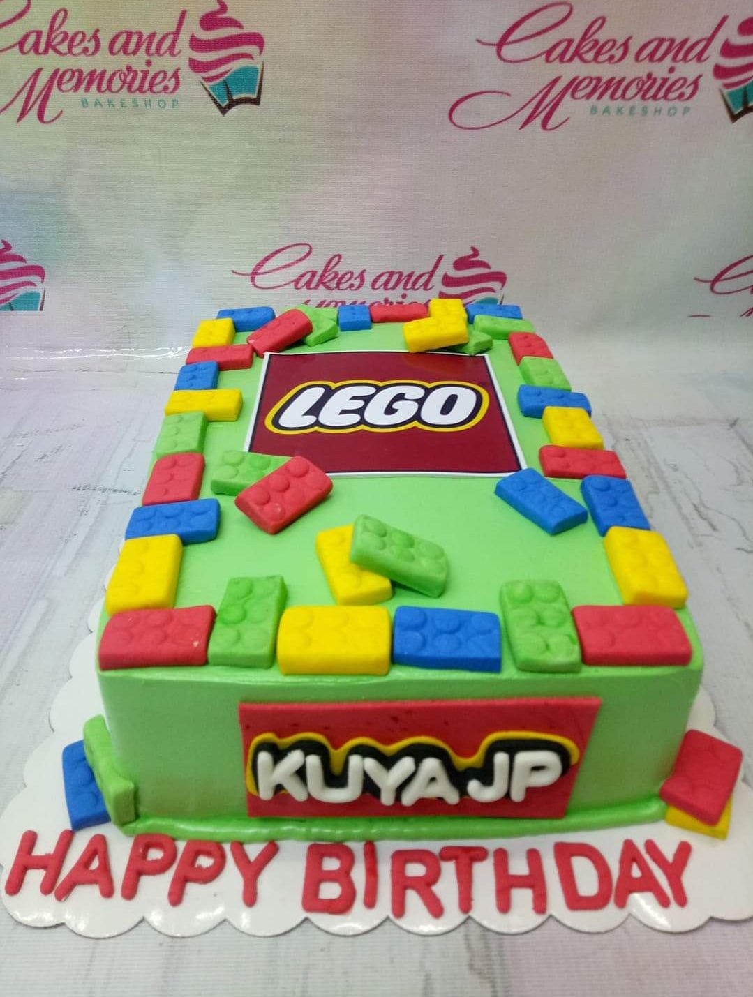 Green Lego-themed rectangle cake with colorful fondant bricks and a Lego logo printout. Green Lego-themed rectangle cake with colorful fondant bricks and a Lego logo printout.