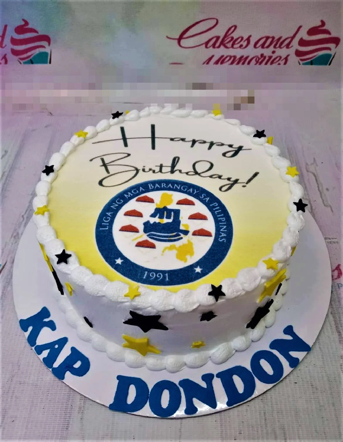 Liga Ng Mga Barangay White Birthday Cake A white 1-tier Liga Ng Mga Barangay cake, with a logo printout, yellow and black stars, and blue gumpaste letters.