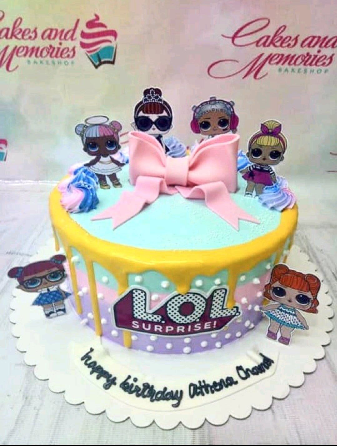 LOL Surprise themed birthday cake with colorful icing drips, character printouts, and a large pink fondant bow. LOL Surprise themed birthday cake with colorful icing drips, character printouts, and a large pink fondant bow.