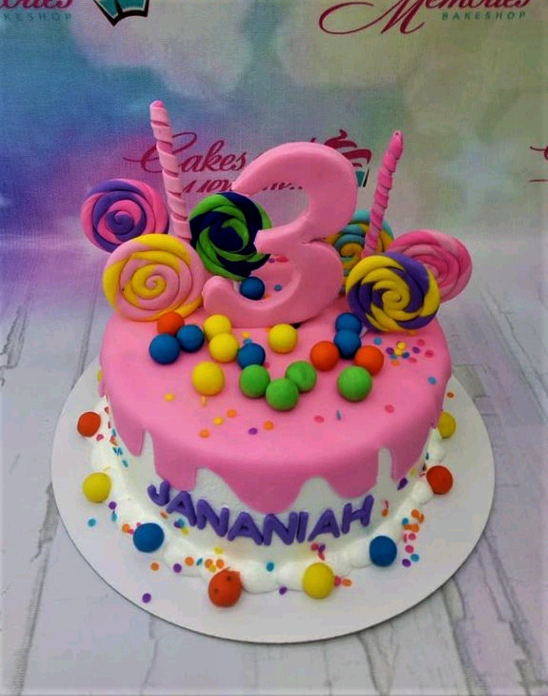 Pink and white lollipop themed birthday cake with colorful candy spheres and a large pink number three topper. Pink and white lollipop themed birthday cake with colorful candy spheres and a large pink number three topper.