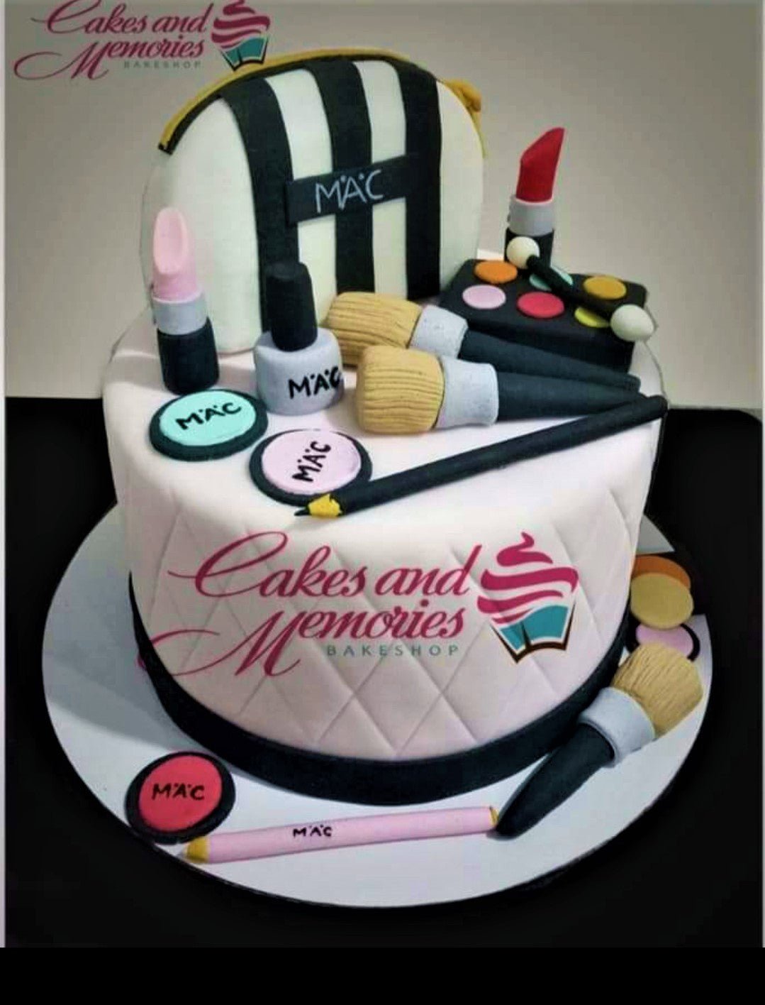 White fondant makeup themed cake with edible 3D MAC cosmetics, brushes, and a striped makeup bag topper. White fondant makeup themed cake with edible 3D MAC cosmetics, brushes, and a striped makeup bag topper.
