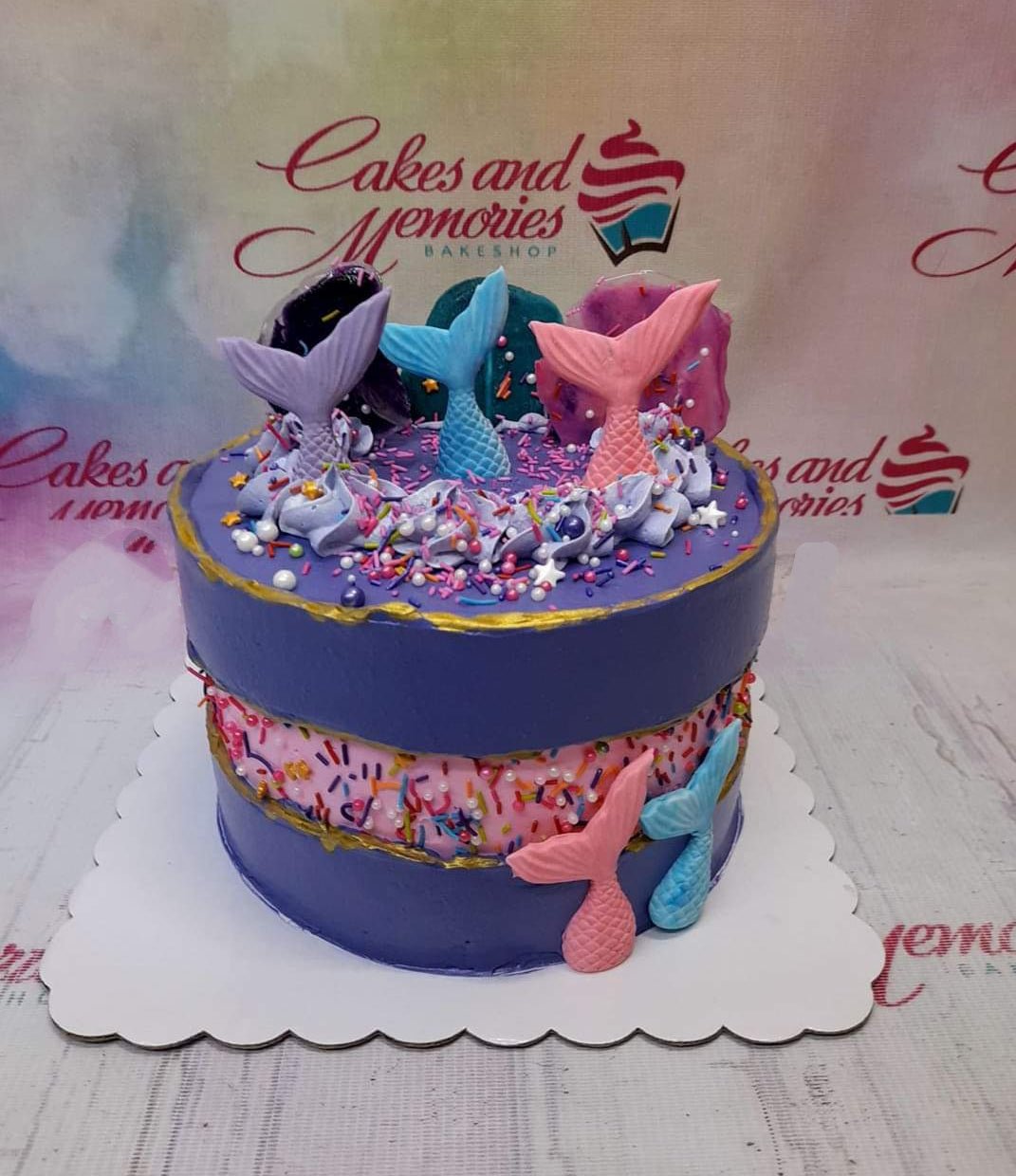 Purple and pink mermaid-themed cake with colorful mermaid tails, isomalt shards, and gold-edged fault line design. Purple and pink mermaid-themed cake with colorful mermaid tails, isomalt shards, and gold-edged fault line design.