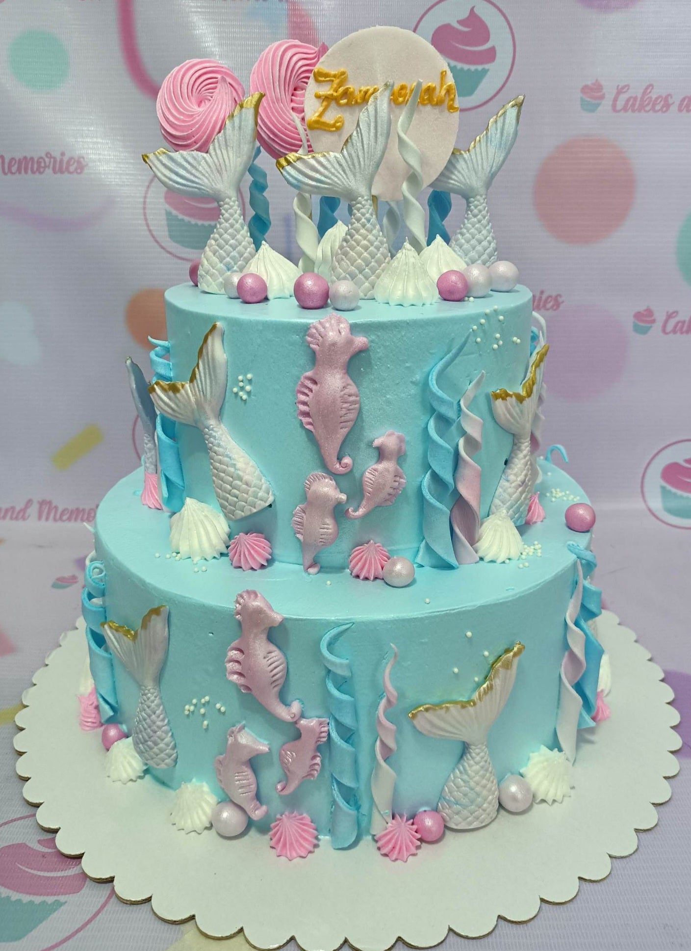 Two-tier light blue mermaid themed cake with pink seahorses, white mermaid tails, and pink meringue pops. Two-tier light blue mermaid themed cake with pink seahorses, white mermaid tails, and pink meringue pops.