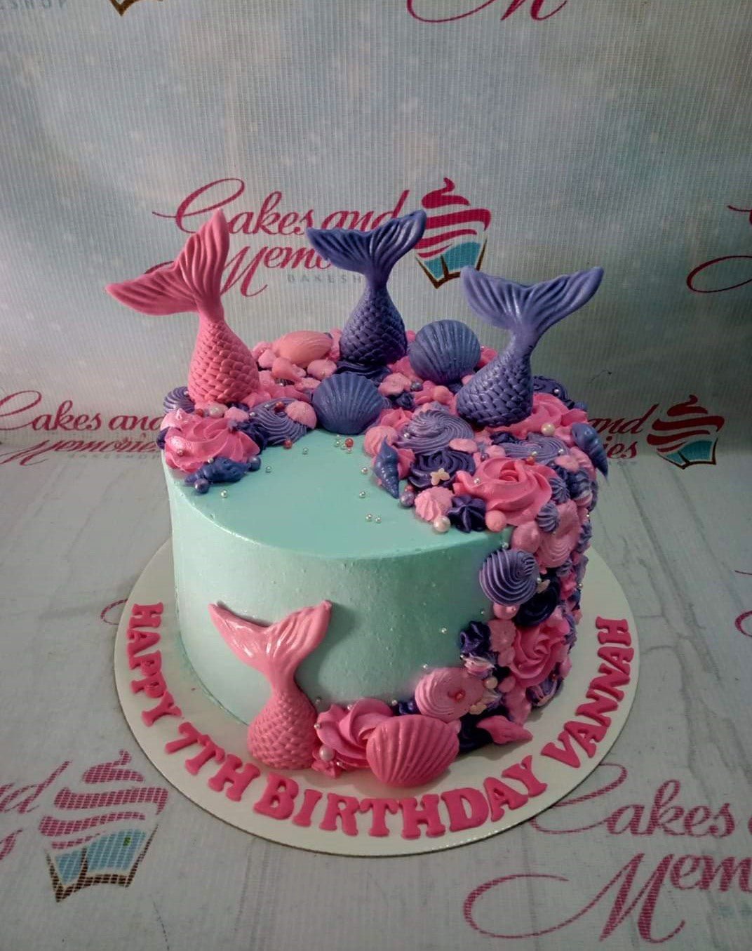 Light blue mermaid themed cake with pink and purple icing rosettes, fondant mermaid tails, and seashells. Light blue mermaid themed cake with pink and purple icing rosettes, fondant mermaid tails, and seashells.