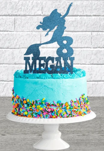 Light blue mermaid birthday cake for Megan with a glittery blue mermaid topper and colorful sprinkles around the base.