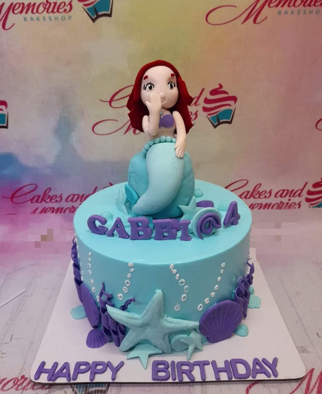 Light blue mermaid themed birthday cake with a 3D Ariel-inspired mermaid topper, purple shells, and a starfish. Light blue mermaid themed birthday cake with a 3D Ariel-inspired mermaid topper, purple shells, and a starfish.