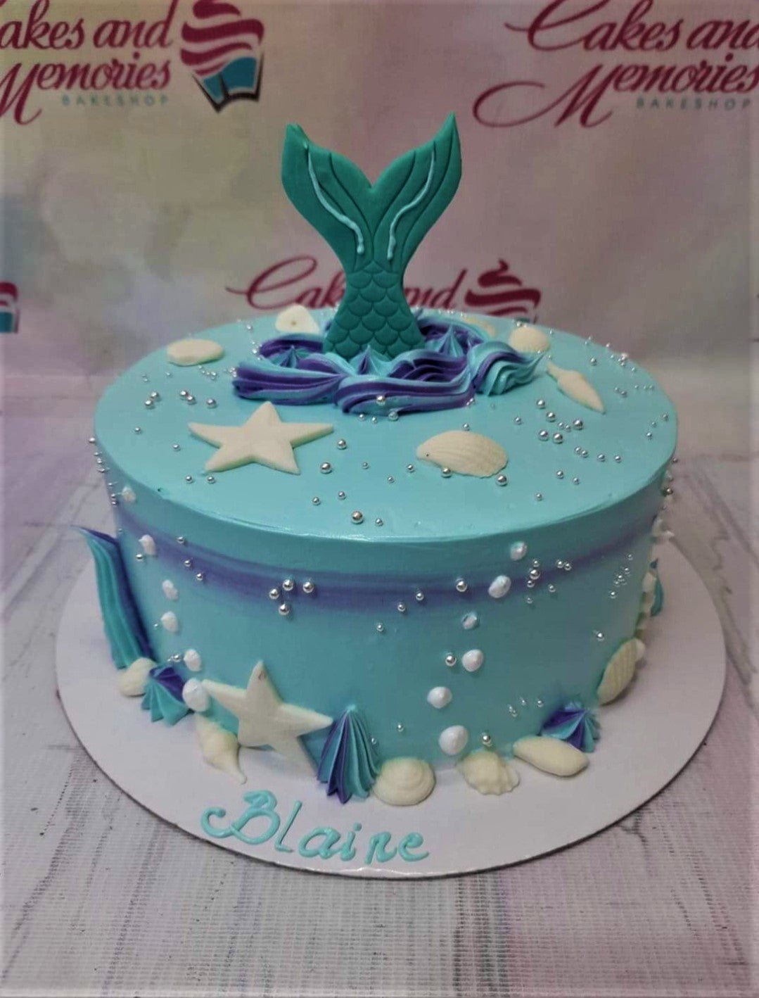 Light blue mermaid themed birthday cake with a teal mermaid tail topper, white starfish, shells, and silver dragees. Light blue mermaid themed birthday cake with a teal mermaid tail topper, white starfish, shells, and silver dragees.