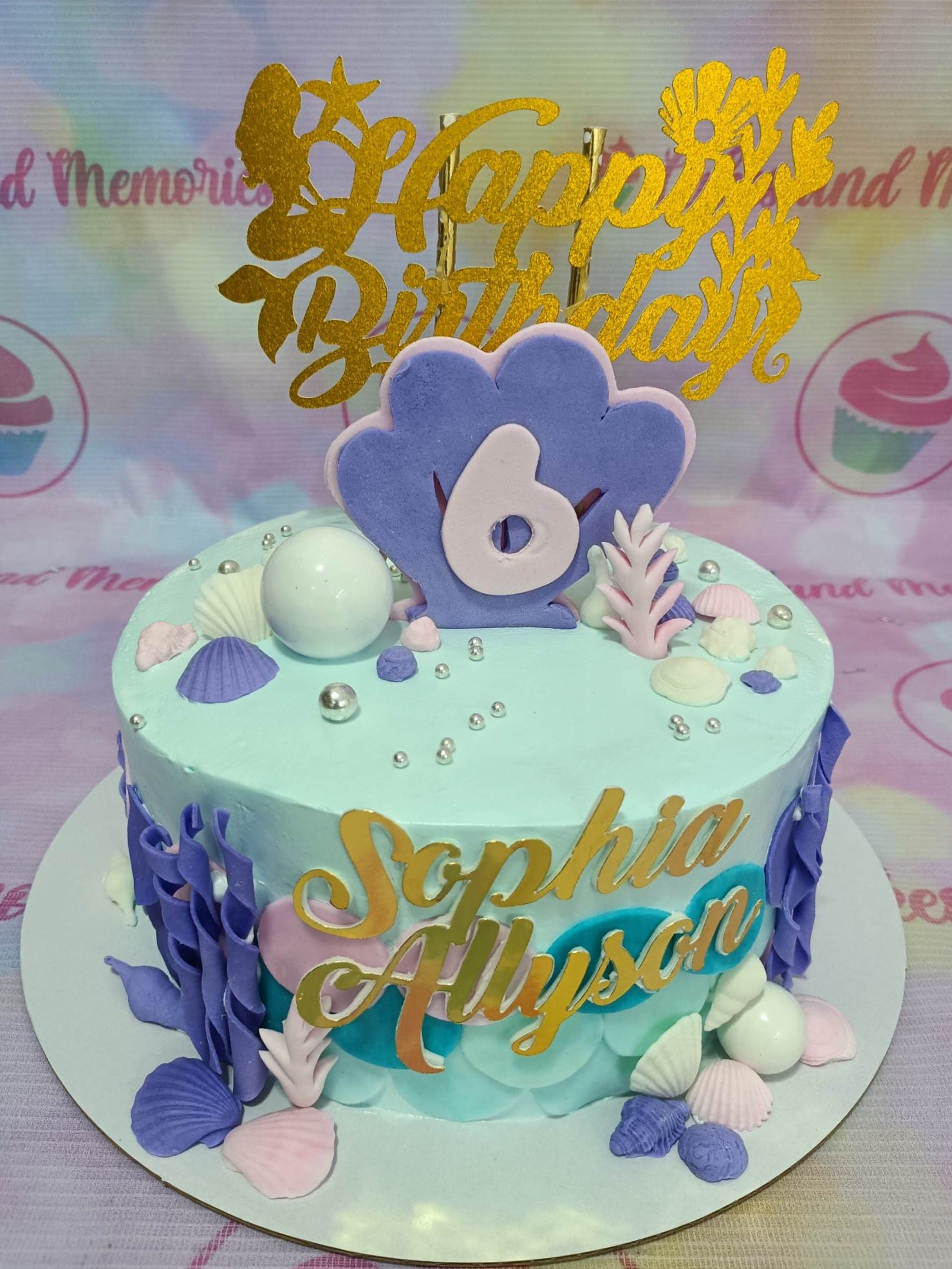 Light blue mermaid themed birthday cake with purple shells, coral, and a gold glitter Happy Birthday topper for Sophia Allyson. Light blue mermaid themed birthday cake with purple shells, coral, and a gold glitter Happy Birthday topper for Sophia Allyson.