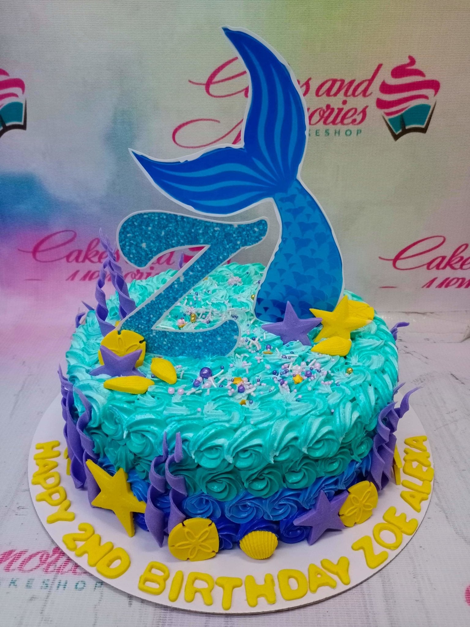 Mermaid themed birthday cake with blue and purple icing rosettes, a large blue mermaid tail topper, and yellow starfish decorations. Mermaid themed birthday cake with blue and purple icing rosettes, a large blue mermaid tail topper, and yellow starfish decorations.