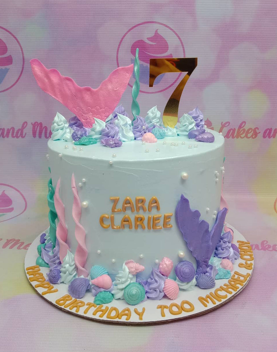 Light blue mermaid themed birthday cake with pink and purple tails, seashells, and a gold number 7 topper. Light blue mermaid themed birthday cake with pink and purple tails, seashells, and a gold number 7 topper.
