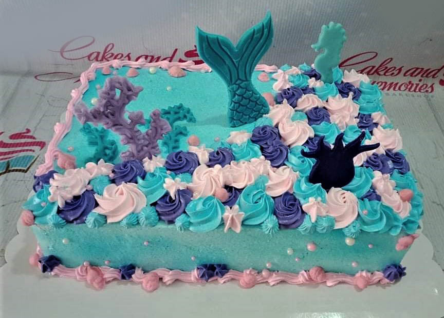 Rectangle mermaid themed cake with light blue icing, pink and purple rosettes, and a large teal mermaid tail topper. Rectangle mermaid themed cake with light blue icing, pink and purple rosettes, and a large teal mermaid tail topper.