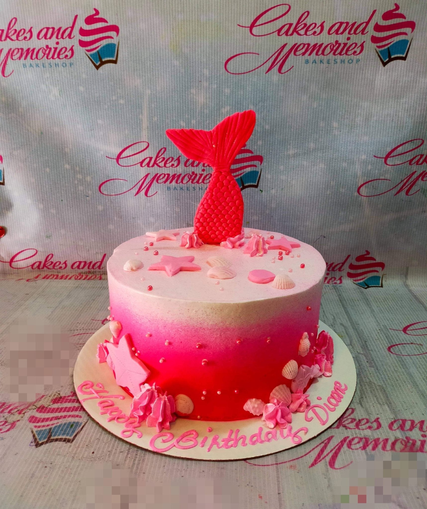 Pink ombre mermaid tail cake with pink fondant stars, seashells, and icing rosettes on a white base board. Pink ombre mermaid tail cake with pink fondant stars, seashells, and icing rosettes on a white base board.