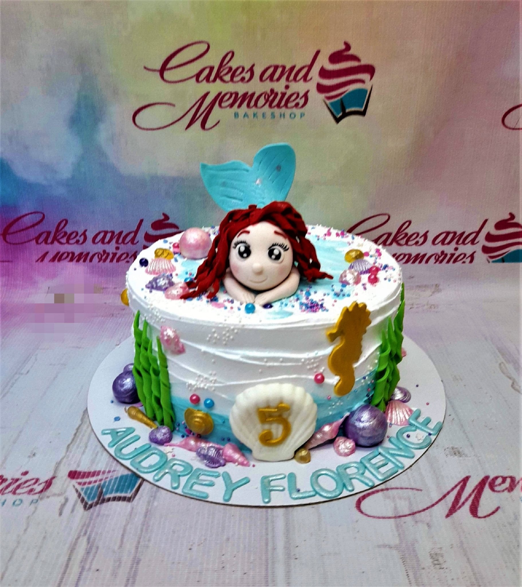 Mermaid themed birthday cake with a 3D fondant mermaid topper, seashells, seahorse, and seaweed decorations on white and blue icing. Mermaid themed birthday cake with a 3D fondant mermaid topper, seashells, seahorse, and seaweed decorations on white and blue icing.