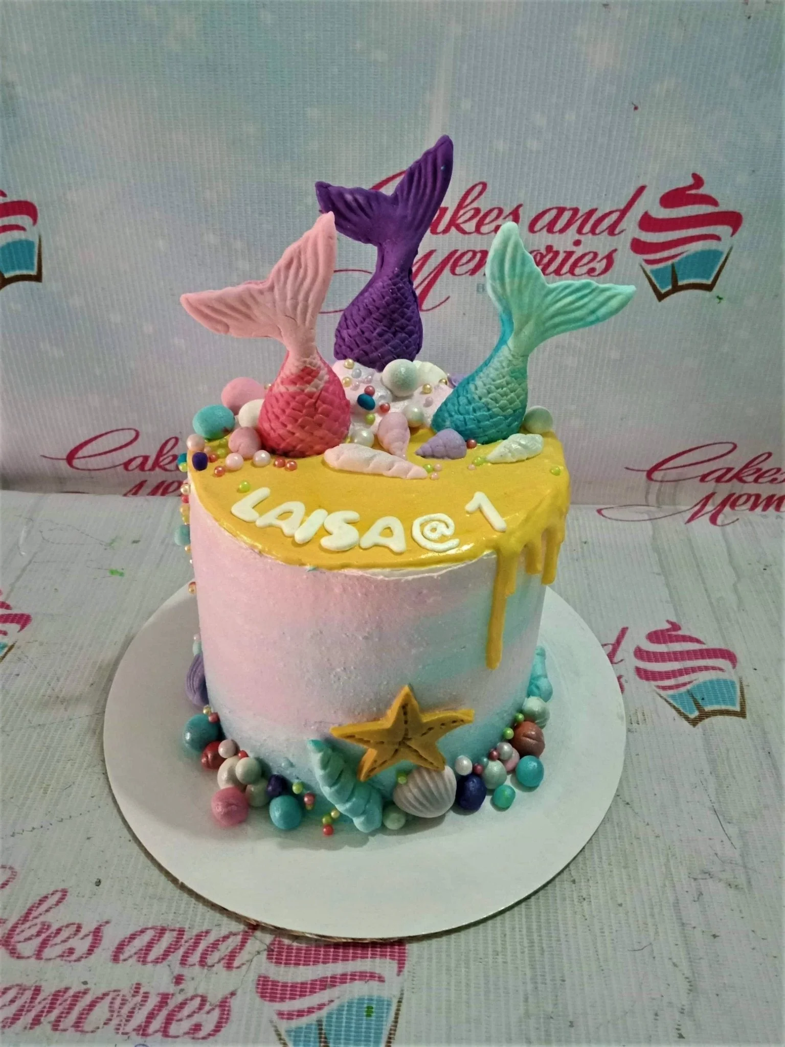 Mermaid Yellow Drip Birthday Cake A blue, pink, and yellow 1 Tier cake themed around Mermaid, featuring mermaid tails, sea shells, and pearls.