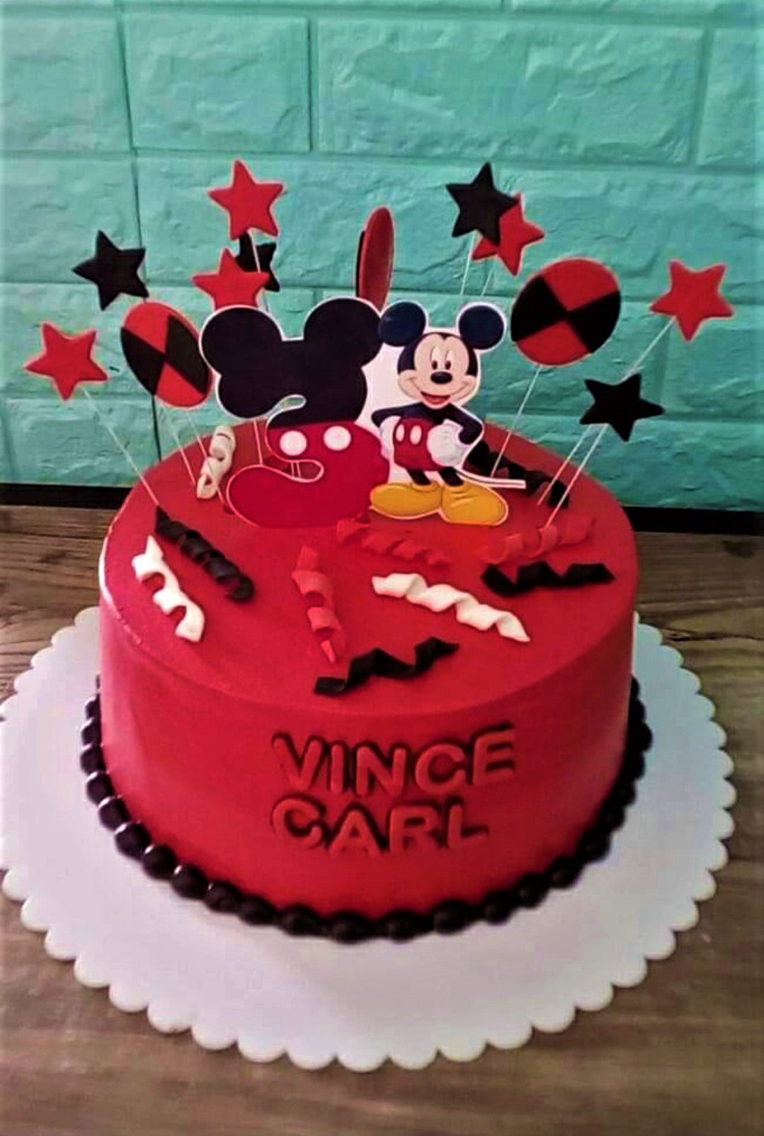 Red Mickey Mouse themed birthday cake with black and red star toppers and a personalized name on the side. Red Mickey Mouse themed birthday cake with black and red star toppers and a personalized name on the side.