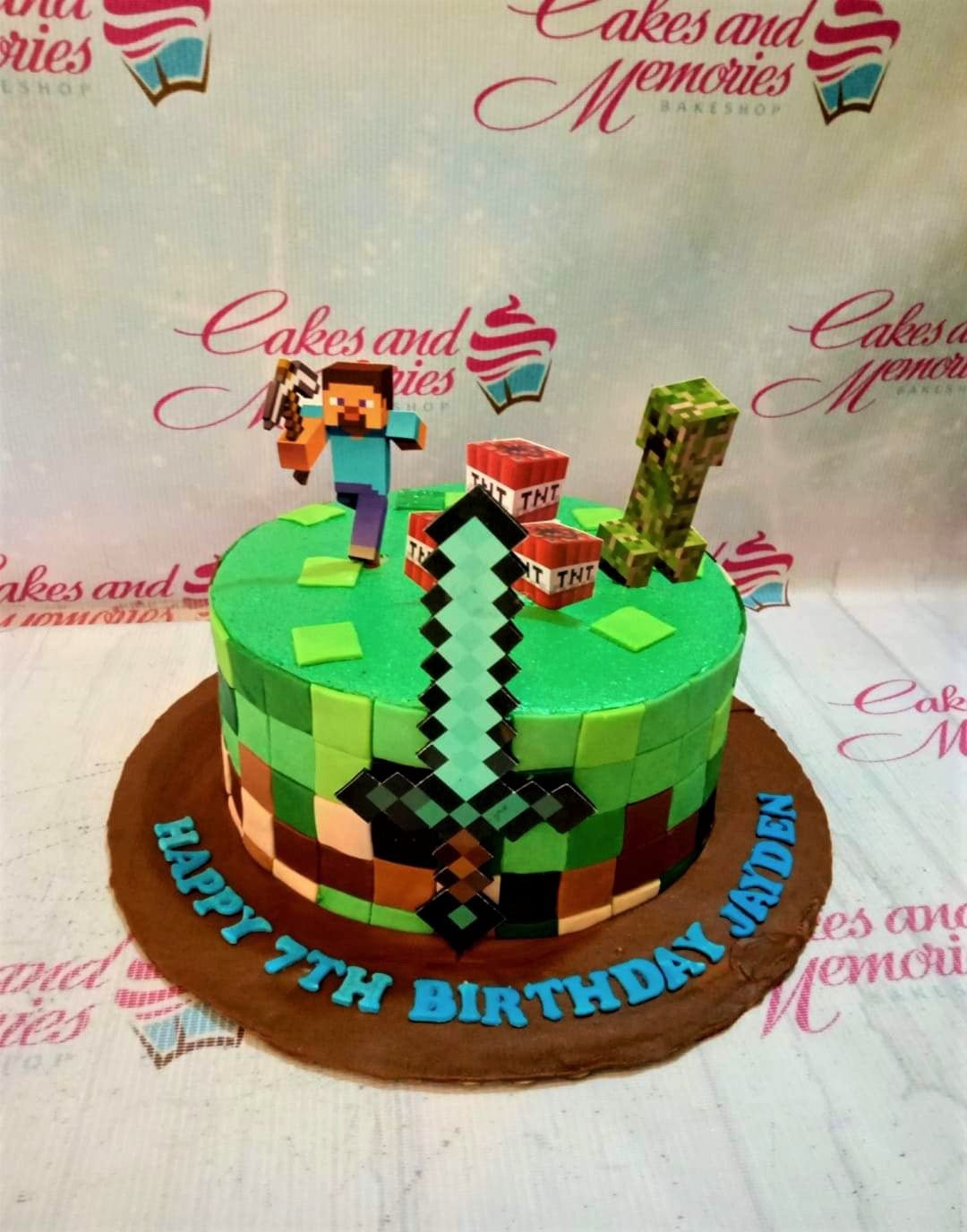 Minecraft themed birthday cake with Steve, Creeper, and TNT toppers on a green and brown pixelated icing base. Minecraft themed birthday cake with Steve, Creeper, and TNT toppers on a green and brown pixelated icing base.
