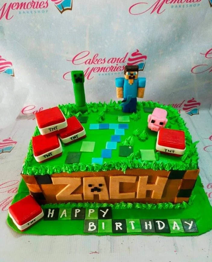 A green and brown square Minecraft cake featuring Steve, Creeper, and pig figures, with TNT blocks, pixelated water, and text.