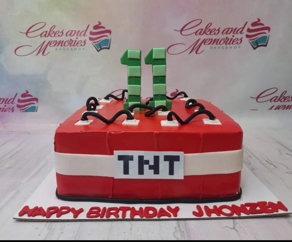 Minecraft-Inspired TNT Cake A red, green, and black square fondant cake themed around Minecraft TNT, featuring pixelated number 11 toppers and black fuse wires.