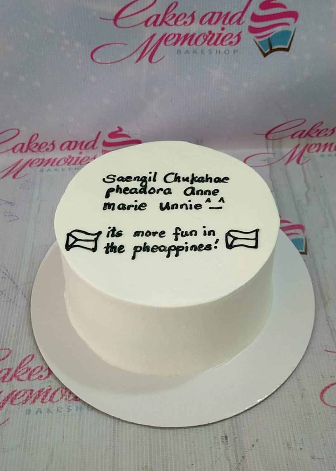 White minimalist bento cake with black piped icing text and envelope doodles on a white base.