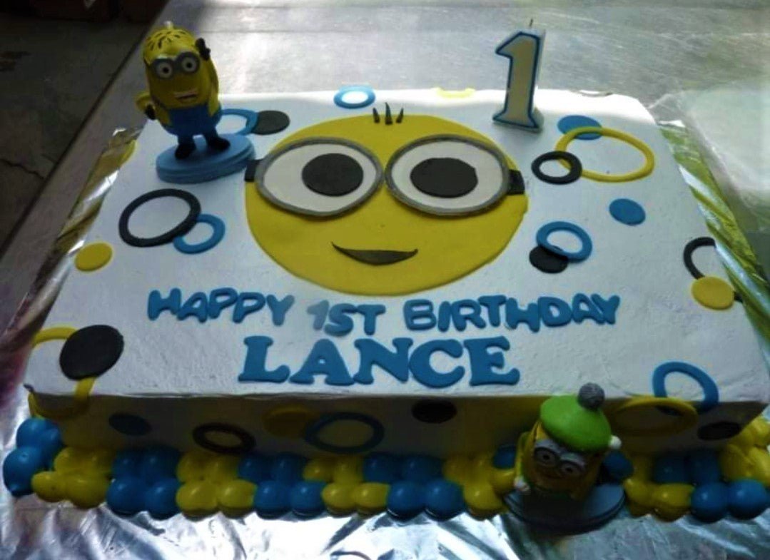Minion themed rectangle birthday cake with yellow minion face icing design and blue and yellow piped borders. Minion themed rectangle birthday cake with yellow minion face icing design and blue and yellow piped borders.