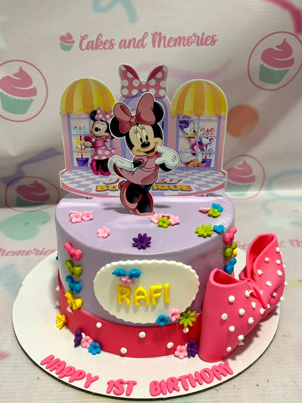 Purple Minnie Mouse birthday cake with a large pink fondant bow and colorful gumpaste flowers.