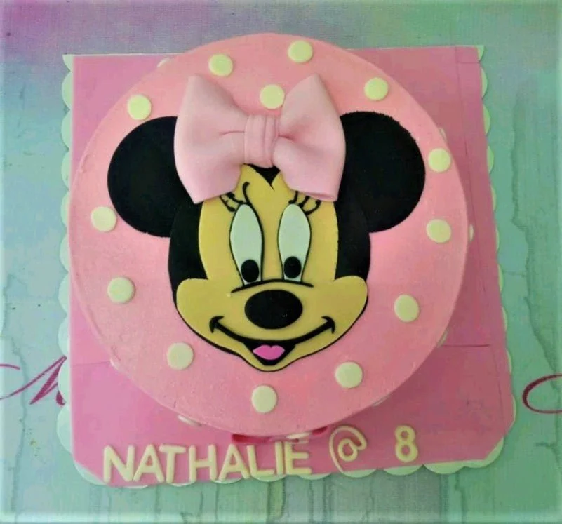 Pink Minnie Mouse themed cake with white polka dots and a large fondant Minnie face with a pink bow.