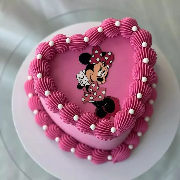 Heart-shaped pink Minnie Mouse cake with intricate hot pink icing ruffles and white sugar pearls.