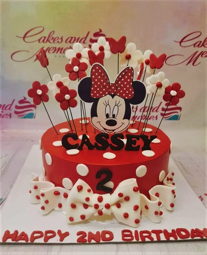 A Red and White 1 Tier cake themed around Minnie Mouse, featuring a Minnie Mouse character, a white fondant bow, and gumpaste flowers.