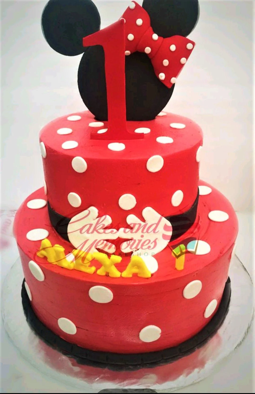 A red, white, and black 2-tier Minnie Mouse cake, with black mouse ears, a red polka dot bow, and a red number one.