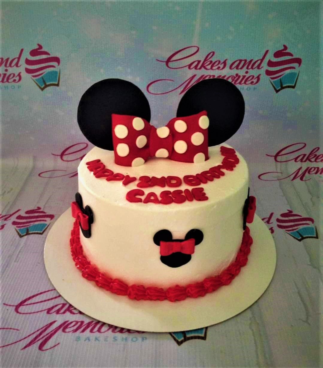 White Minnie Mouse themed birthday cake with a large red polka dot bow, black ears, and red icing border. White Minnie Mouse themed birthday cake with a large red polka dot bow, black ears, and red icing border.