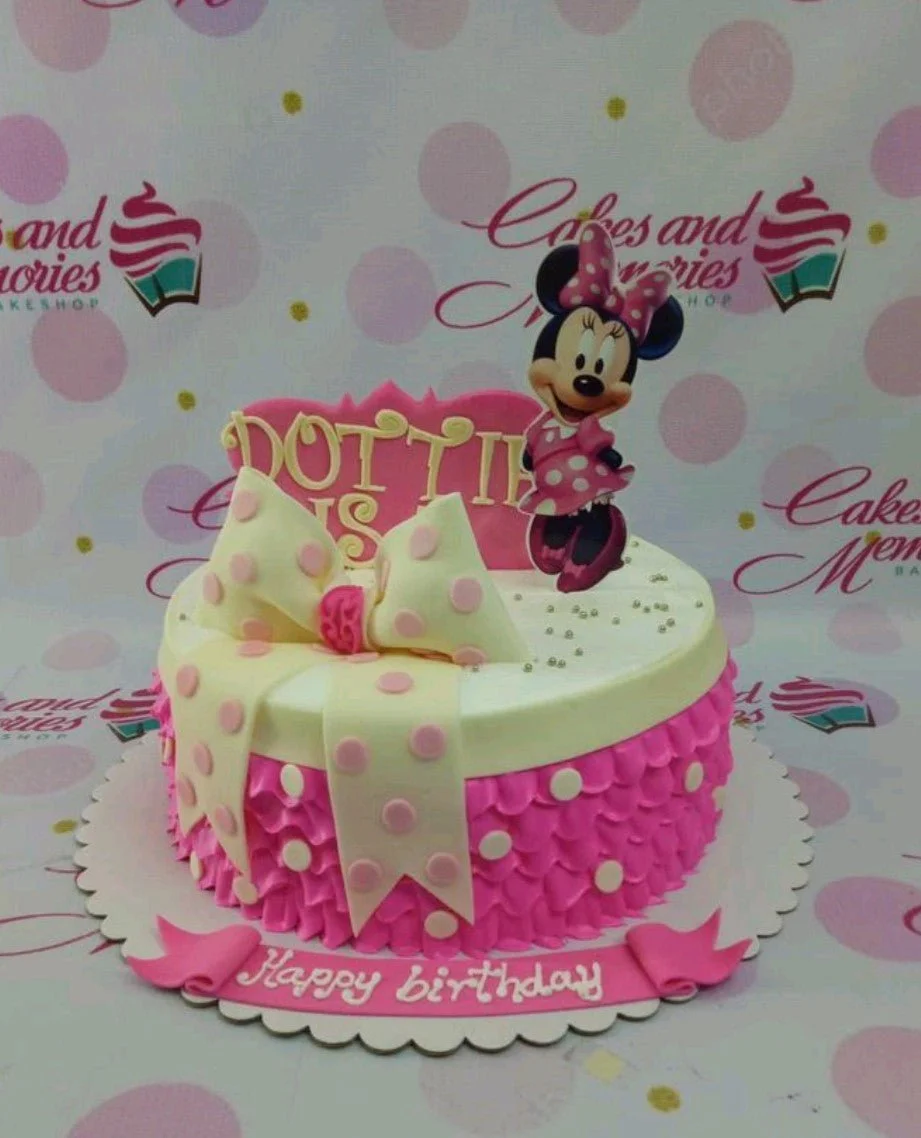Pink Minnie Mouse birthday cake with a large polka dot bow, pink ruffles, and a Minnie Mouse printout topper.