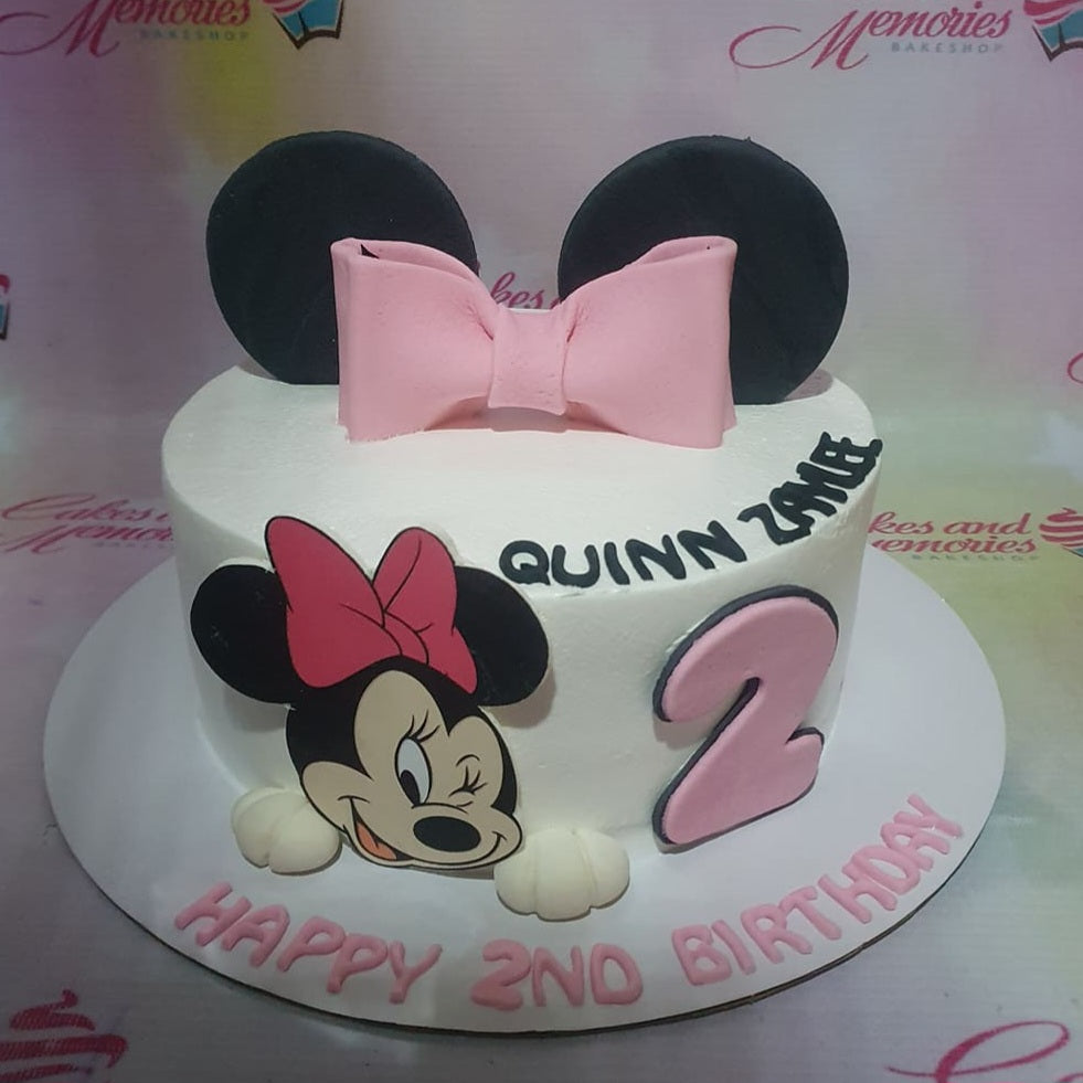 White Minnie Mouse themed birthday cake with large pink fondant bow, black ears, and a Minnie Mouse printout on the side. White Minnie Mouse themed birthday cake with large pink fondant bow, black ears, and a Minnie Mouse printout on the side.