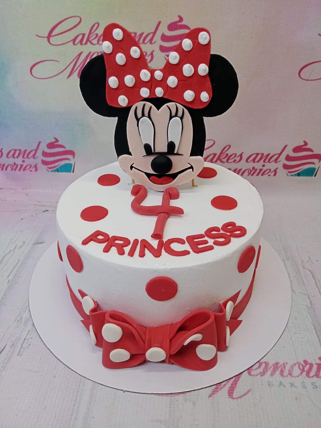 White Minnie Mouse birthday cake with red polka dots, a large Minnie Mouse printout topper, and a red fondant bow. White Minnie Mouse birthday cake with red polka dots, a large Minnie Mouse printout topper, and a red fondant bow.