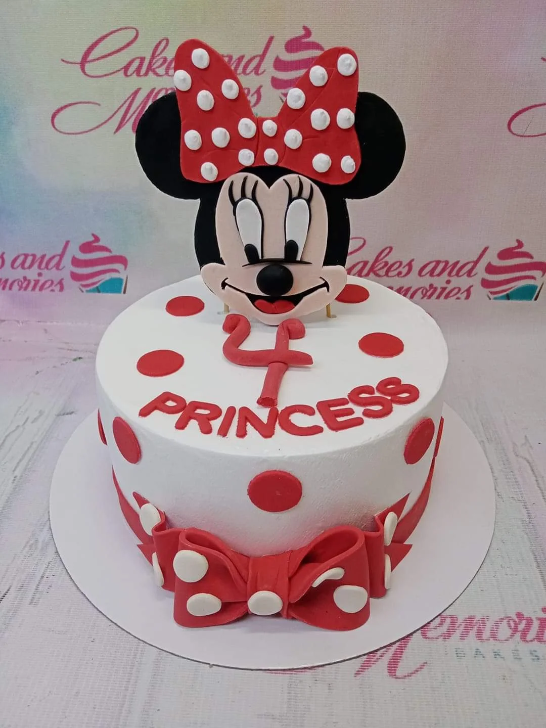 White Minnie Mouse birthday cake with red polka dots, a large Minnie Mouse printout topper, and a red fondant bow.