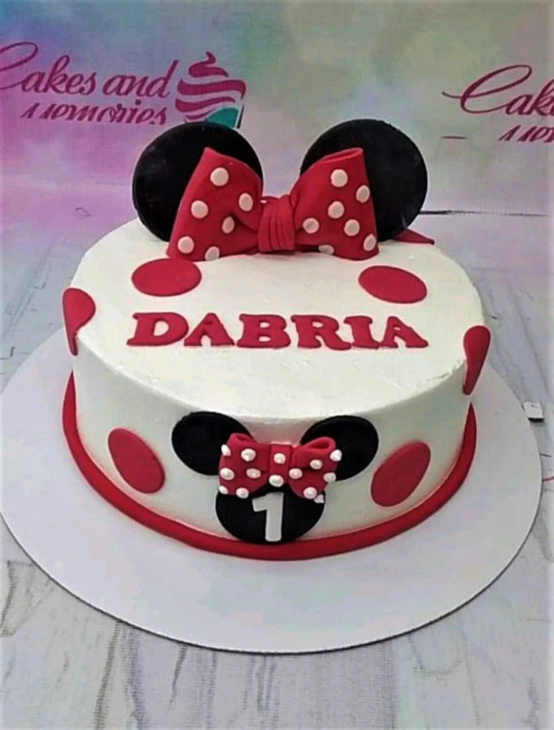 White Minnie Mouse themed birthday cake with red polka dots and a large red fondant bow on top.