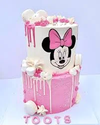 Two-tier Minnie Mouse themed cake with pink and white icing, pink drips, and marshmallow decorations.