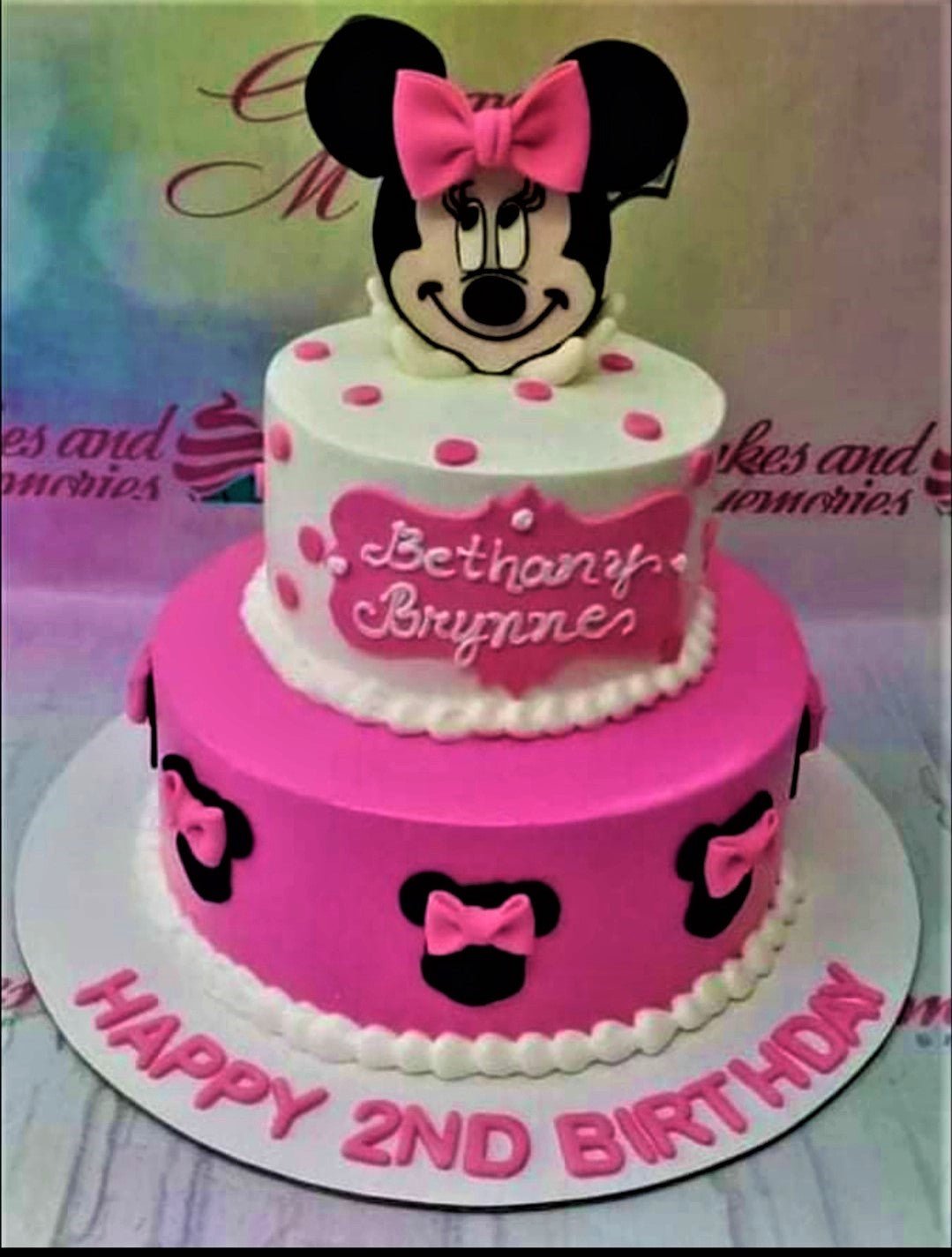 Two-tier pink and white Minnie Mouse themed birthday cake with fondant bows and a large Minnie Mouse topper. Two-tier pink and white Minnie Mouse themed birthday cake with fondant bows and a large Minnie Mouse topper.