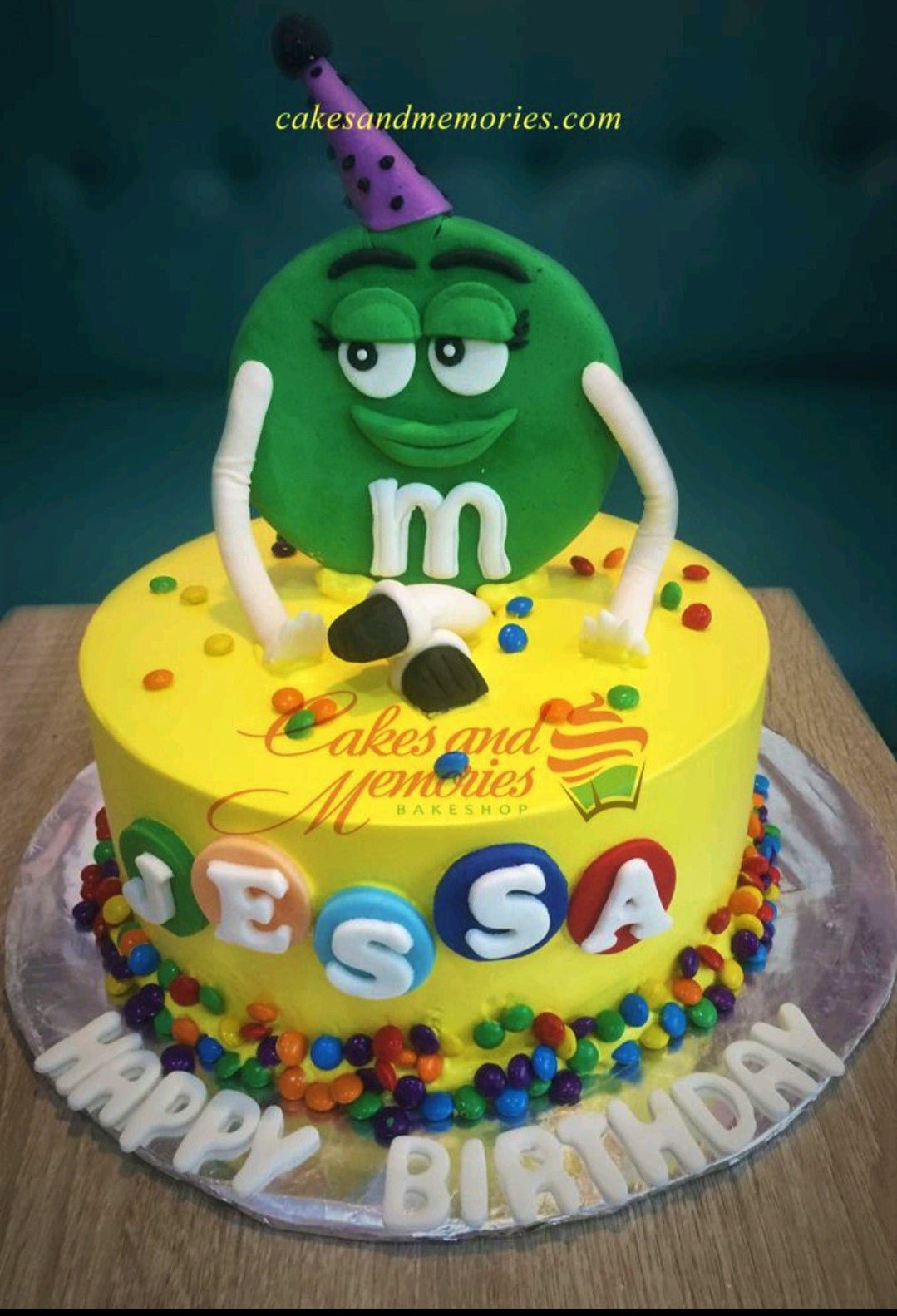 Yellow M&M character birthday cake with colorful chocolate candies and gumpaste name letters Yellow M&M character birthday cake with colorful chocolate candies and gumpaste name letters