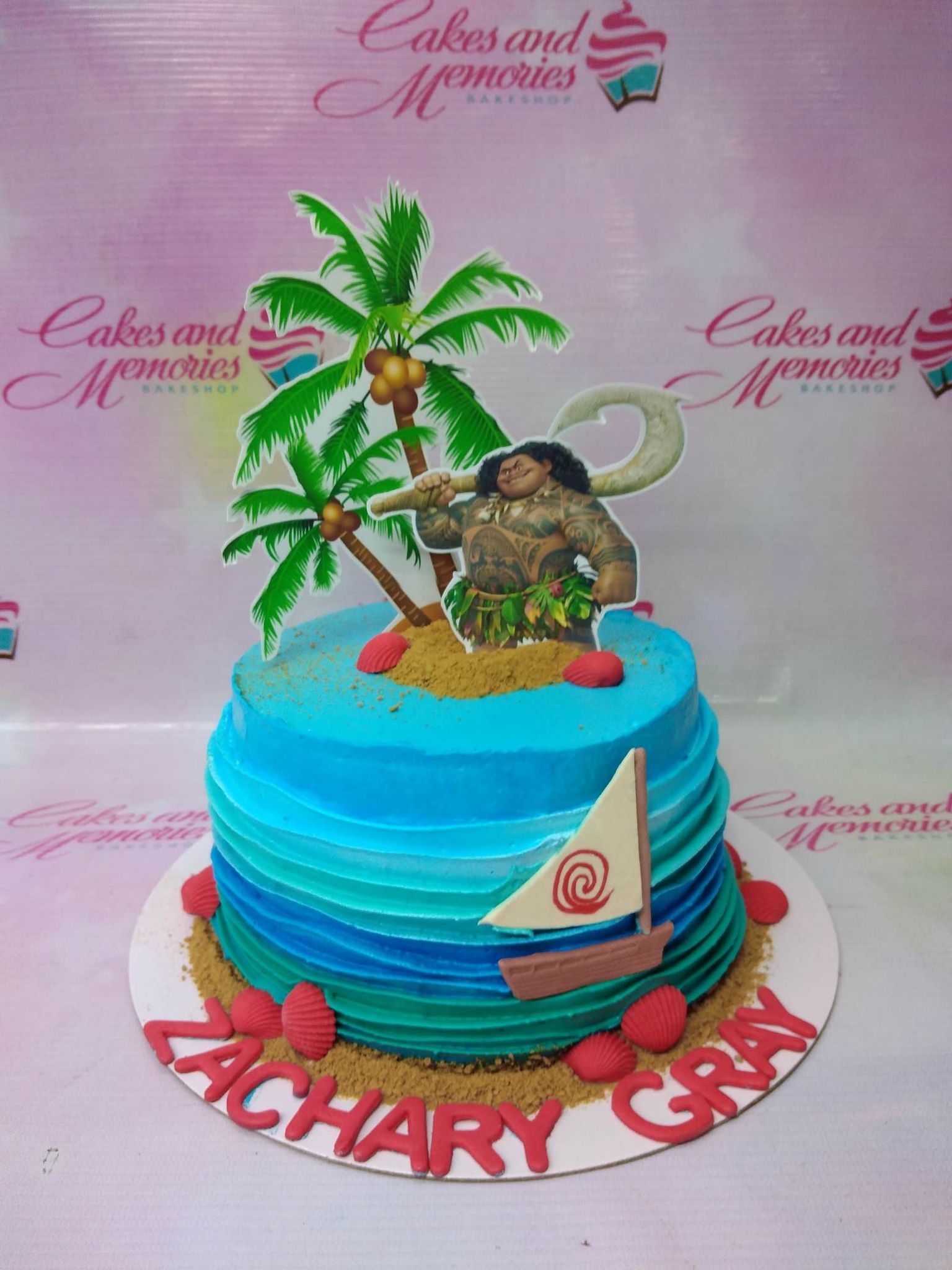 Moana themed blue ocean cake with Maui printout topper, palm trees, and a sailboat on a sandy base. Moana themed blue ocean cake with Maui printout topper, palm trees, and a sailboat on a sandy base.