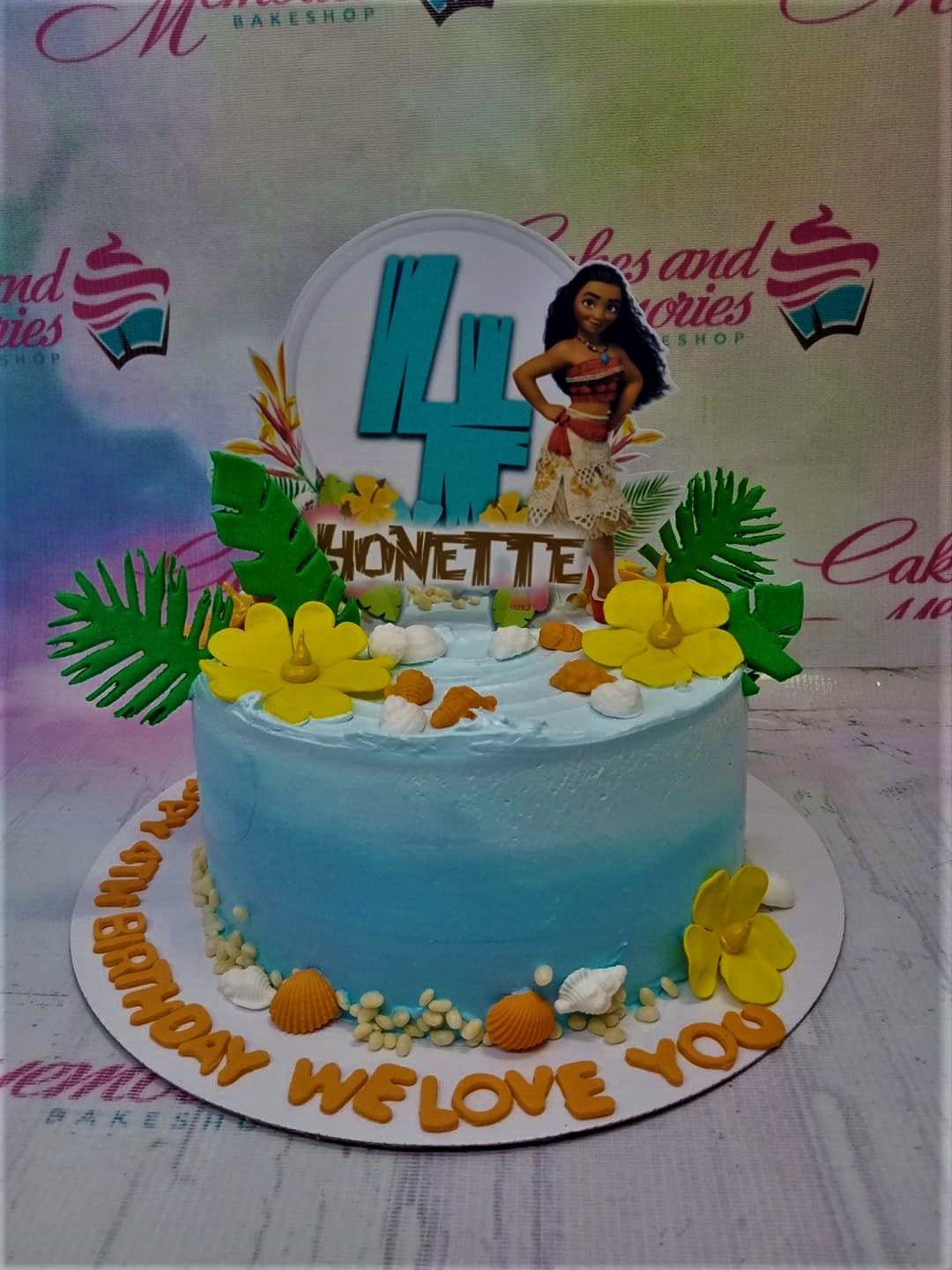 Moana themed blue gradient cake with tropical leaves, yellow flowers, seashells, and a Moana character printout topper. Moana themed blue gradient cake with tropical leaves, yellow flowers, seashells, and a Moana character printout topper.